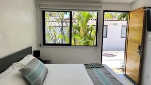 Ein Schlafzimmer mit Bett, Kissen, einem Nachttisch, einem Fenster und einer offenen Tür, die nach draußen führt.