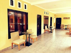 A hotel lobby with a long corridor, multiple doors, and seating areas with tables and chairs.