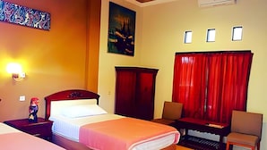 A hotel room with a bed, a desk, a chair, a wardrobe, and a painting on the wall. - Hotel Sentral (Buleleng)