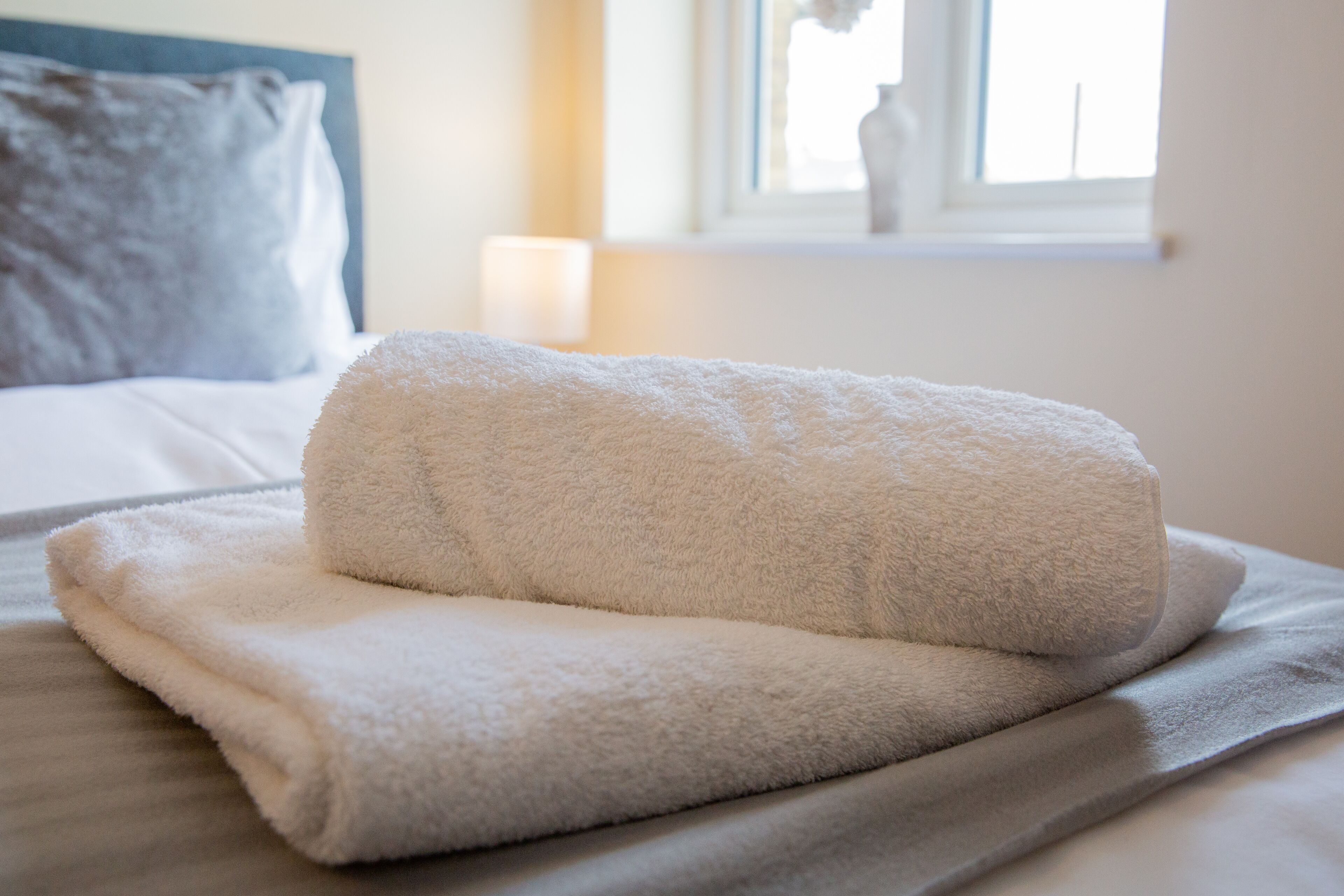 A neatly folded white towel on a bed with a gray blanket.