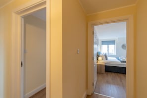 Un couloir menant à une chambre à coucher équipée d’un lit, d’une table de chevet et d’une fenêtre.