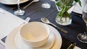A dining table set with white plates, a bowl, a spoon, and a glass of water. - 2-bedroom Penthouse, Clockhouse, Hoddesdon (Hoddesdon)