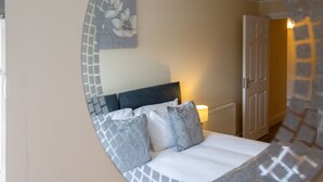 A bedroom with a bed, pillows, a headboard, a wall with a floral painting, and a door. - 2-bedroom Penthouse, Clockhouse, Hoddesdon (Hoddesdon)