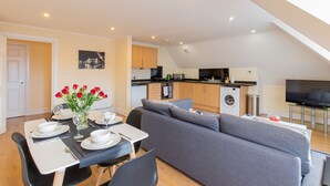 A modern apartment with a dining area, grey sofa, kitchen, and a TV. - 2-bedroom Penthouse, Clockhouse, Hoddesdon (Hoddesdon)