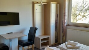 A hotel room with a bed, a desk, a chair, a wardrobe, and a television. - Pension Zum Adler (Hünstetten)