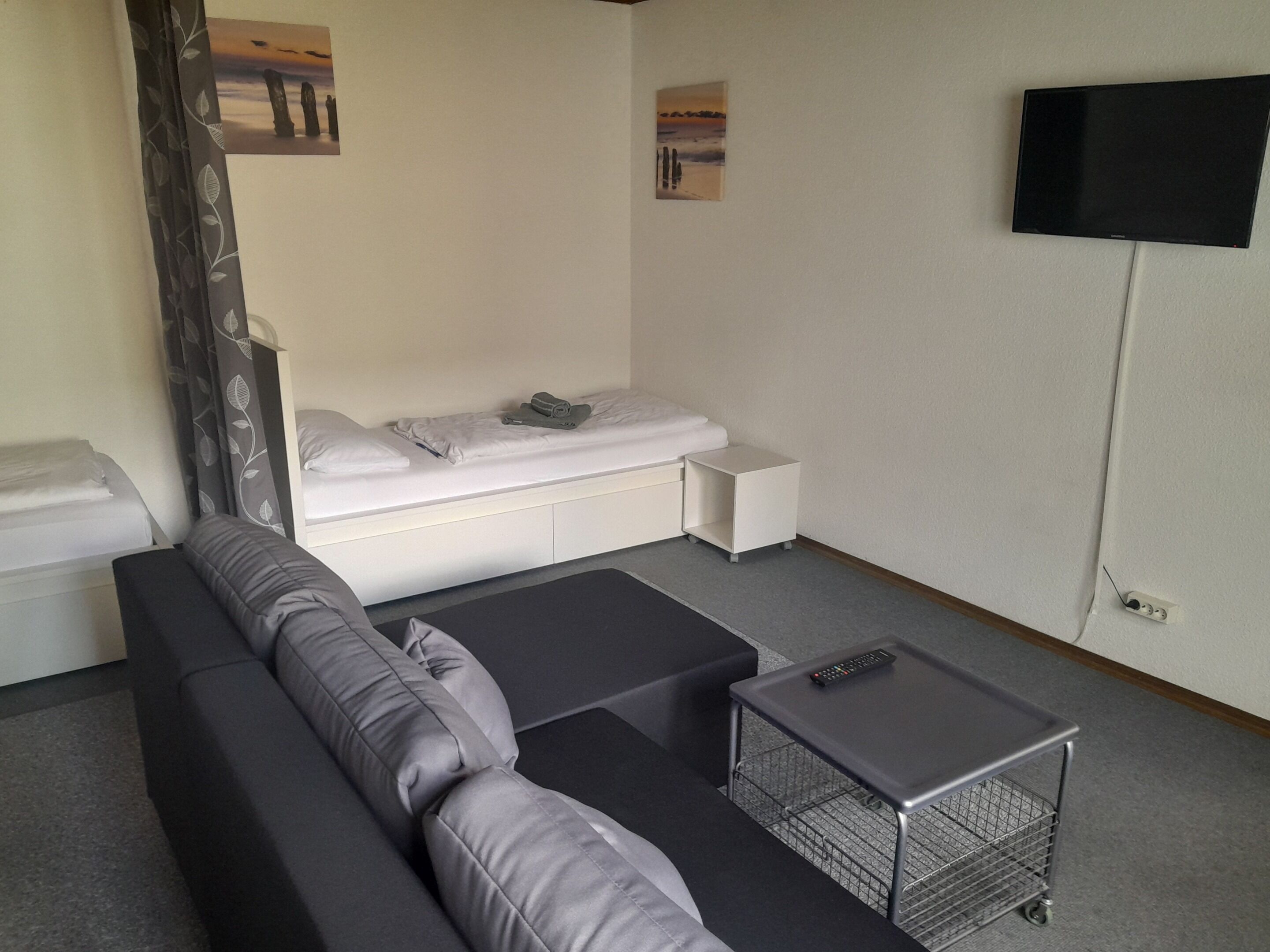 Et lille hotelværelse med seng, sofa, et lille bord og et fjernsyn på væggen.