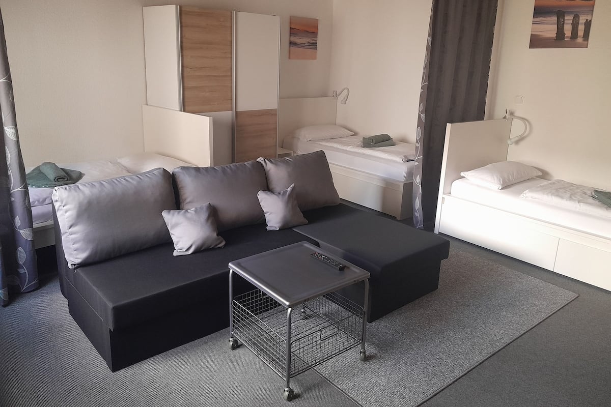 A modern hotel room with a black sofa, a small table, a bed, and a bathroom.