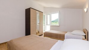 A bedroom with two beds, a wardrobe, and a window with a view of greenery. - Stunning apartment in Hodilje with house sea view (Hodilje)