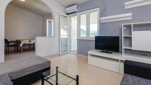 A modern living room with a flat-screen TV, a dining area with a table and chairs, and a balcony with a view of the mountains. - Stunning apartment in Hodilje with house sea view (Hodilje)