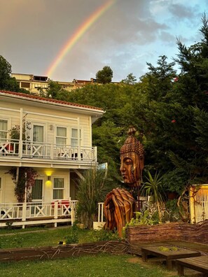 Un edificio con balcón, una gran estatua de Buda y un arcoíris en el cielo.