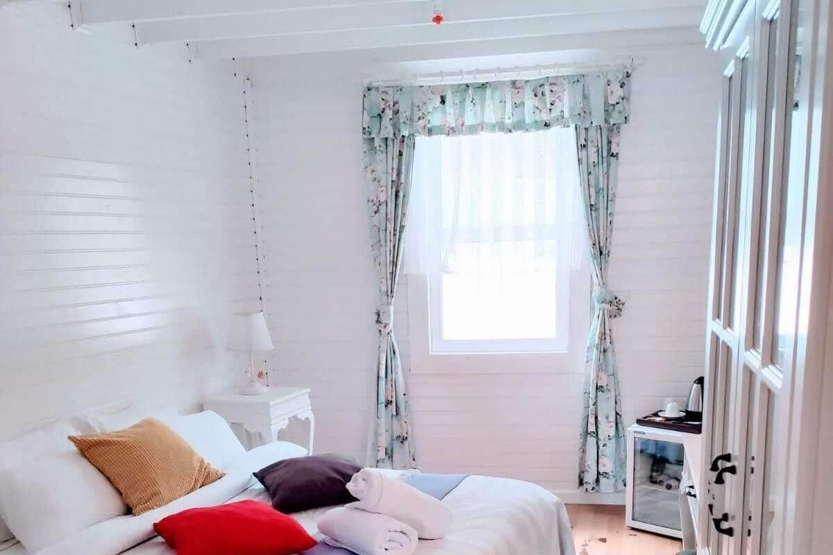 A bedroom with a bed, a nightstand, a window with curtains, and a wooden floor.