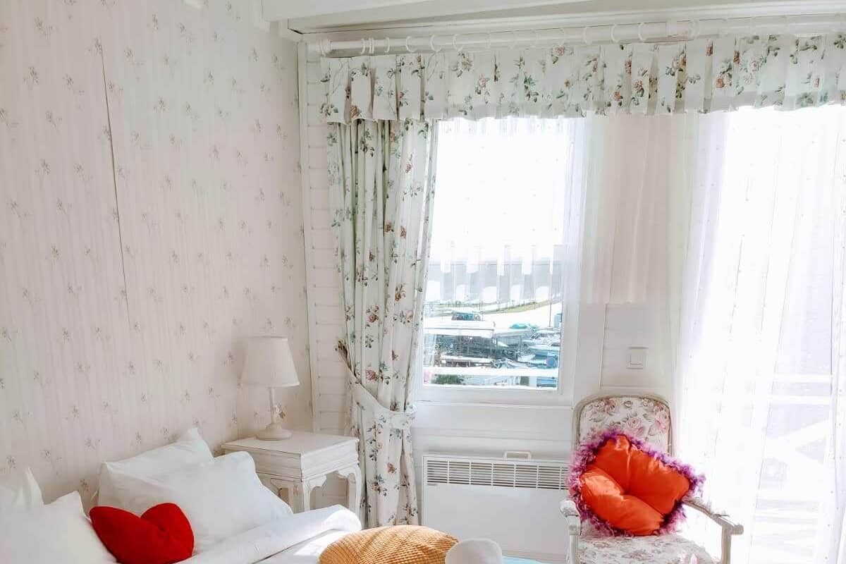A neatly arranged bedroom with a bed, pillows, a chair, and a view of the city through the window.