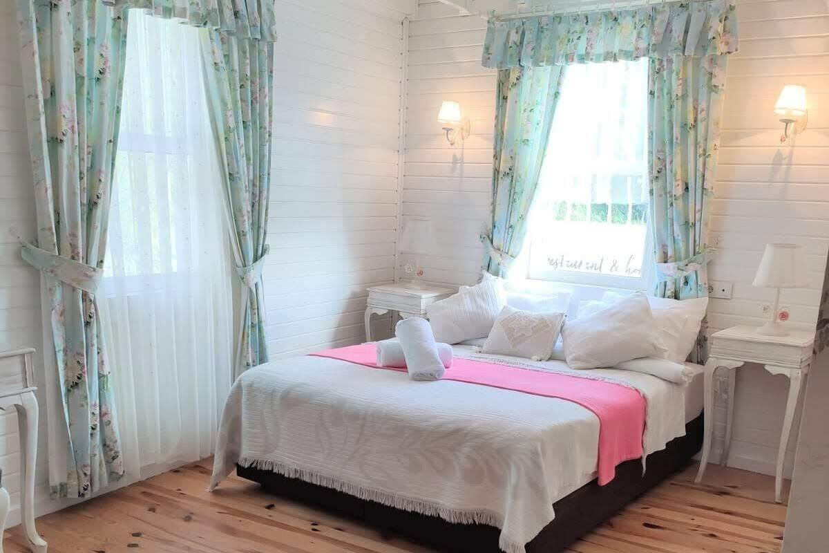 A bedroom with a bed, two bedside tables, a nightstand, a rug, and floral curtains.