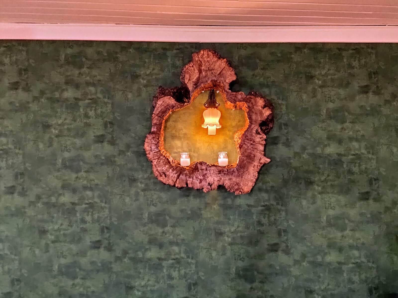 A wooden wall decoration with a central light fixture and two small candles.