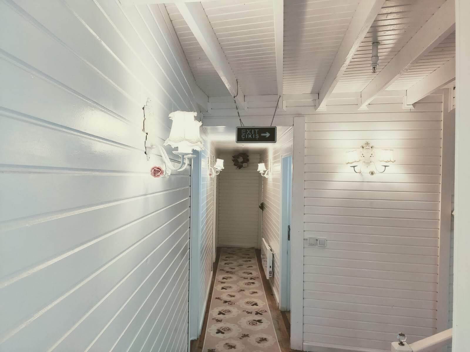 A narrow hallway with white walls and a floral patterned floor. An exit sign is visible in the distance.