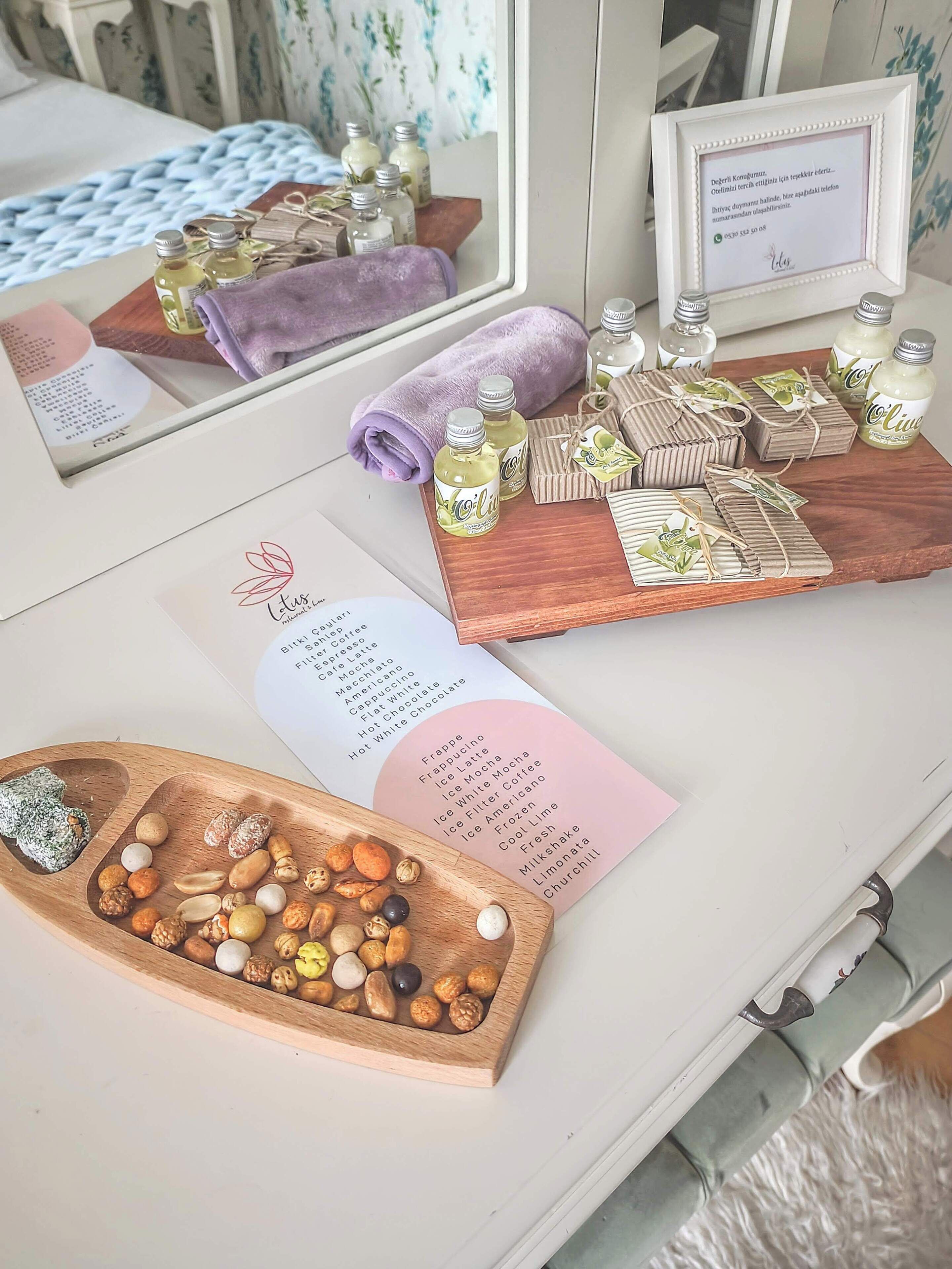Una mesa ordenada con diversos elementos, como botellas, una bandeja de madera con frutos secos, un menú y una nota enmarcada.