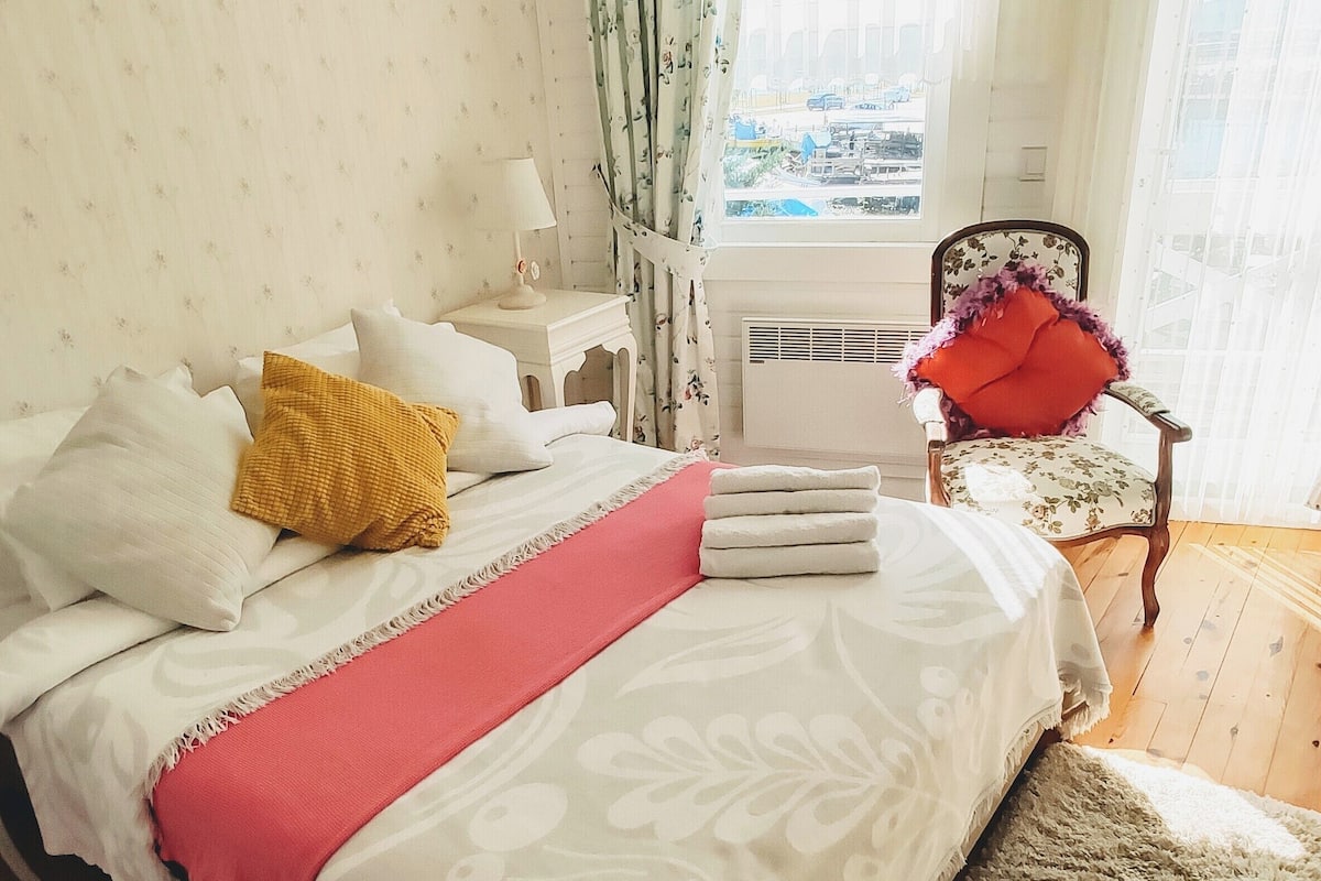 A bedroom with a bed, a chair, a window, and a view of the city.