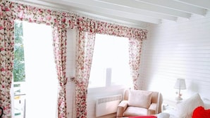 Un dormitorio con cama, una silla, un escritorio y una ventana con cortinas florales.
