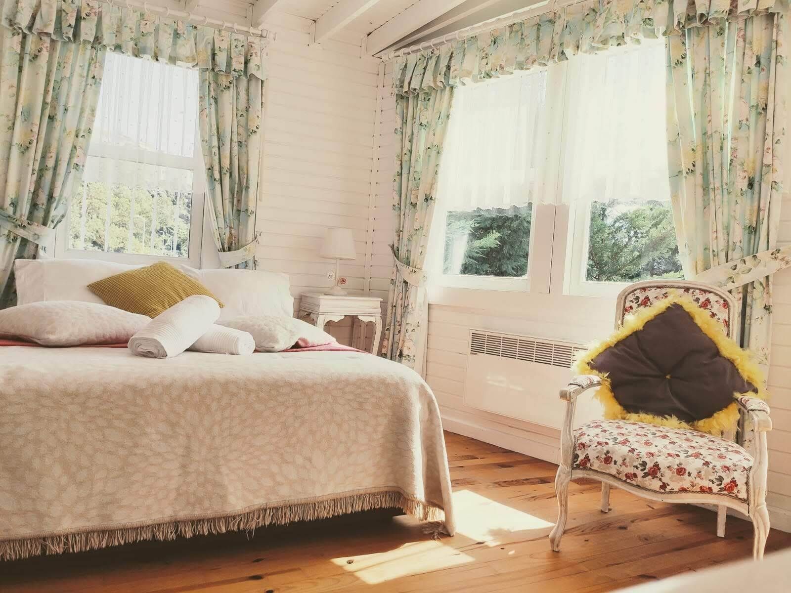 Un dormitorio con cama, una silla, una mesita de noche y una ventana con cortinas.