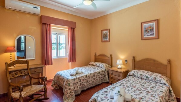 A bedroom with two single beds, a wooden chair, a desk, a mirror, and a window with curtains. - Hacienda el Corchuelo Marchena by Ruralidays (Seville)