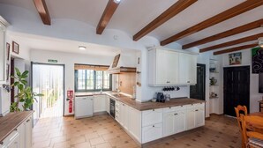 A kitchen with white cabinets, wooden beams, a herringbone floor pattern, and a view to the outside.
