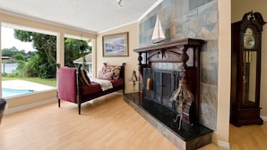 A spacious living room with a fireplace, a large clock, and a view of a swimming pool. - Riverfront Retreat. Private Oasis 7 minutes to downtown (Jacksonville)