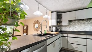 A modern kitchen with white cabinets, a black countertop, and a backsplash. There is a sink, a clock, and a potted plant on the counter. - Riverfront Retreat. Private Oasis 7 minutes to downtown (Jacksonville)