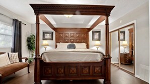 A four-poster bed with a wooden headboard, a bedside table with a lamp, and a large mirror on the wall. - Riverfront Retreat. Private Oasis 7 minutes to downtown (Jacksonville)