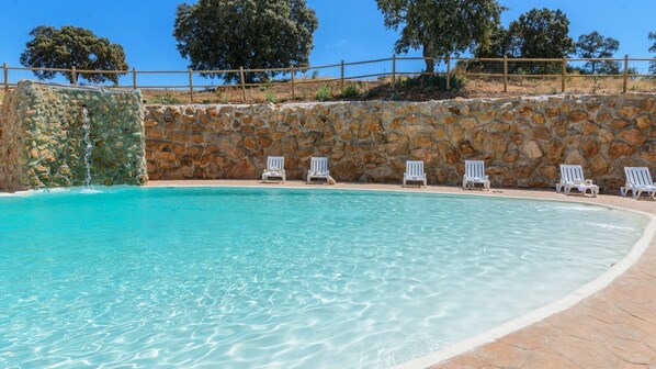 A clear swimming pool with a stone wall and white lounge chairs along the edge. - Casa Rural San Miguel Morón de la Frontera by Ruralidays (Seville)
