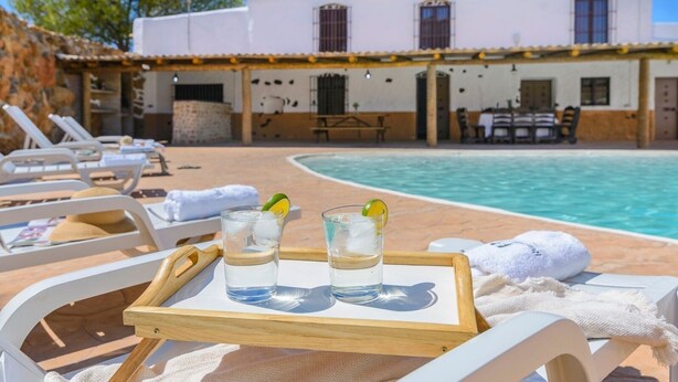 Ein Poolbereich mit Liegestühlen und einem Tablett mit zwei Gläsern Wasser und Limettenscheiben.
