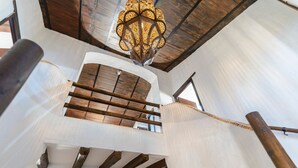 Ein modernes Interieur mit einer Holztreppe, einer dekorativen Deckenleuchte und Blick durch ein Fenster.