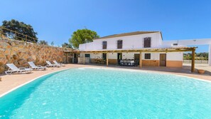 Una piscina con lettini, una zona patio coperta e un edificio con muro in pietra e tetto in tegole.