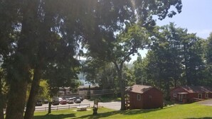 A grassy area with a picnic table, a small brick building, and a parking lot with cars. - The Gold Eagle Cabin (Lake George)