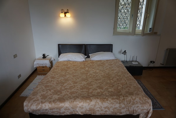 Quarto com cama grande, mesa de cabeceira, abajur e janela com vista.
