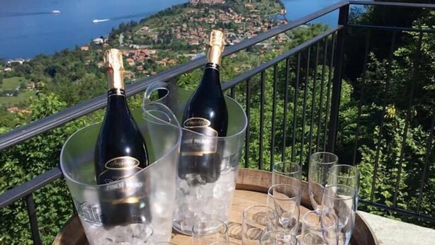 A scenic view of a lake with mountains in the background, a wooden barrel with wine bottles and glasses on a balcony railing. - App.with garden, WI-FI free, automatic gate, covered garage, air conditioning  (Bellagio)