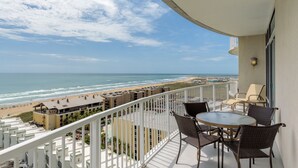 Ein Balkon mit Korbstühlen und einem Tisch mit Blick auf einen Strand und den Ozean.