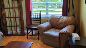 A cozy living room with a leather sofa, wooden coffee table, and a view of greenery through the window. - Saltbox cottage (Clarke's Beach)