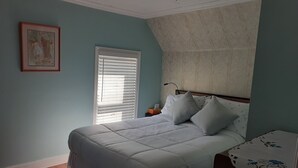 A bedroom with a bed, a nightstand, a window with blinds, a ceiling fan, and a framed picture on the wall. - Saltbox cottage (Clarke's Beach)