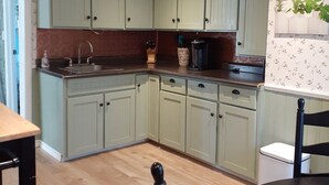 A kitchen with light green cabinets, a wooden floor, and a black dining table. - Saltbox cottage (Clarke's Beach)