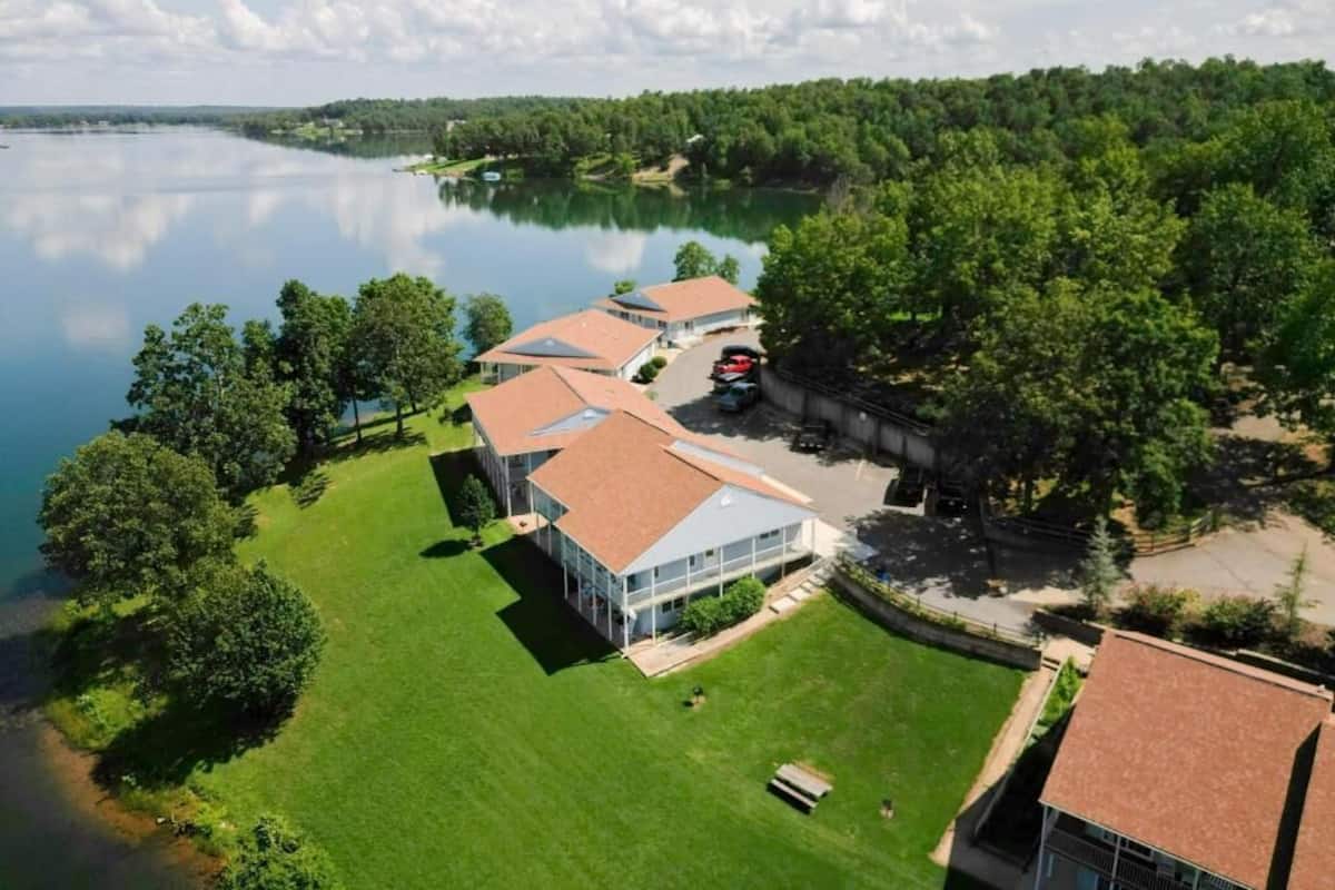Une propriété située au bord d’un lac, comprenant plusieurs bâtiments, un espace de stationnement et une pelouse bien entretenue.