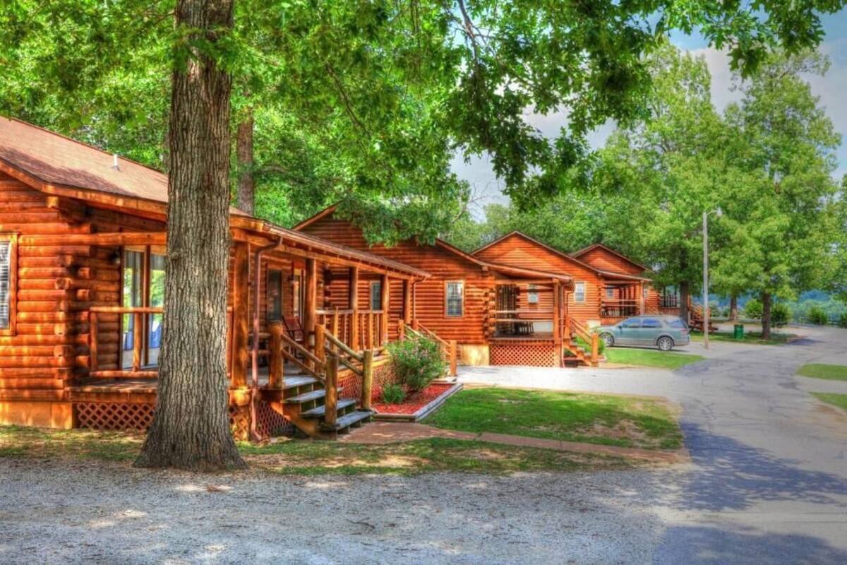 Une rangée de chalets en rondins, avec une allée de gravier et une voiture garée à proximité.