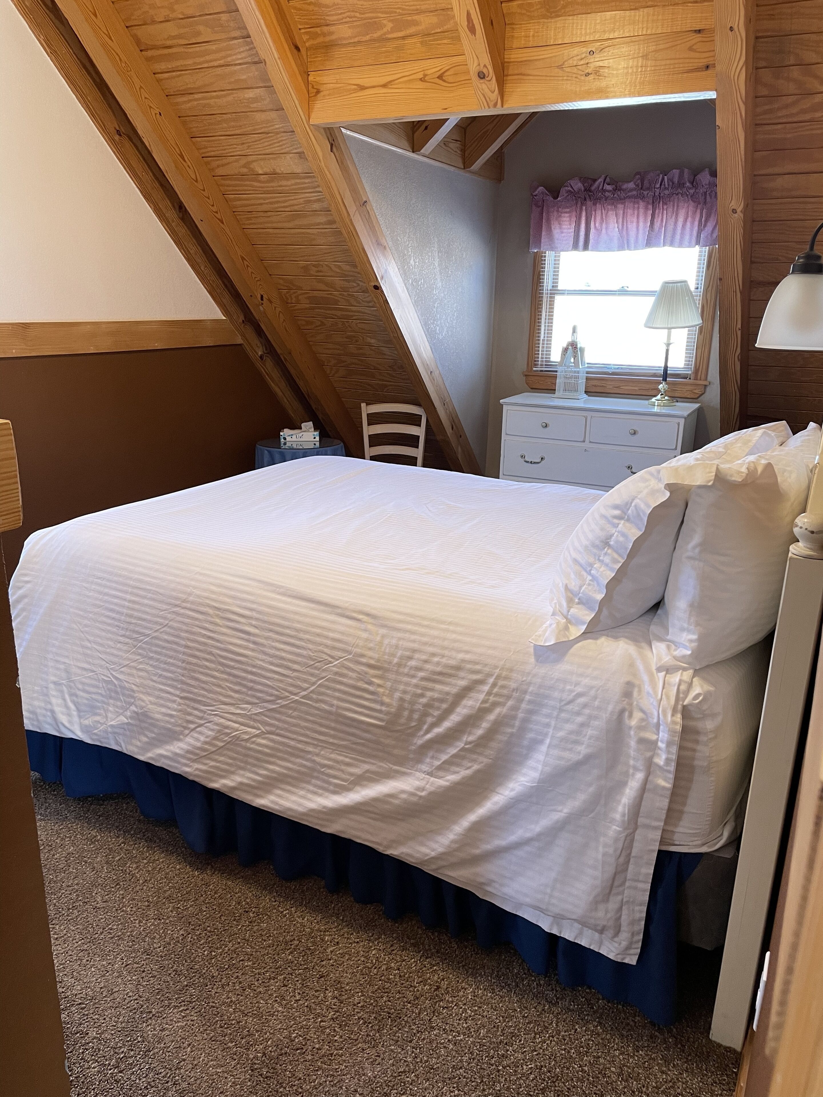 A bedroom with a bed, a nightstand, a chair, a dresser, and a window with curtains.