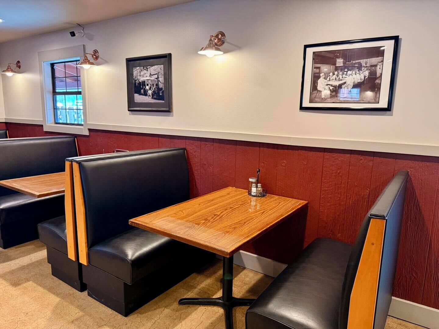 A restaurant interior with booths, tables, framed black and white photos on the wall, and pendant lighting.