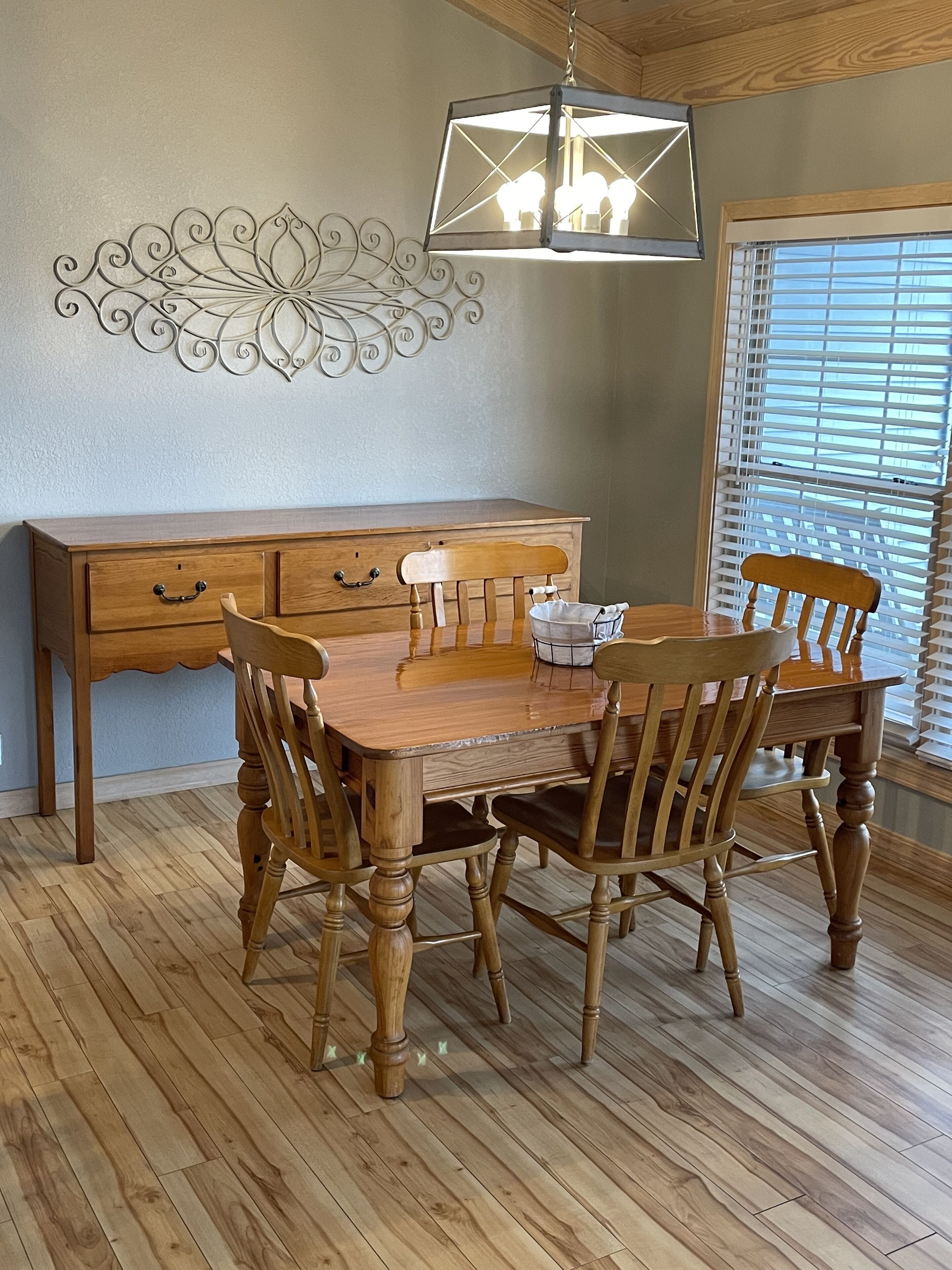 A dining room with a wooden table and chairs, a wooden cabinet with drawers, and a decorative wall piece.
