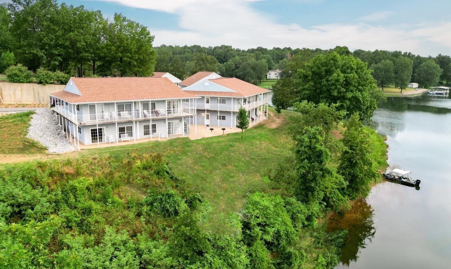 A large, two-story house with a balcony, situated by a lake.