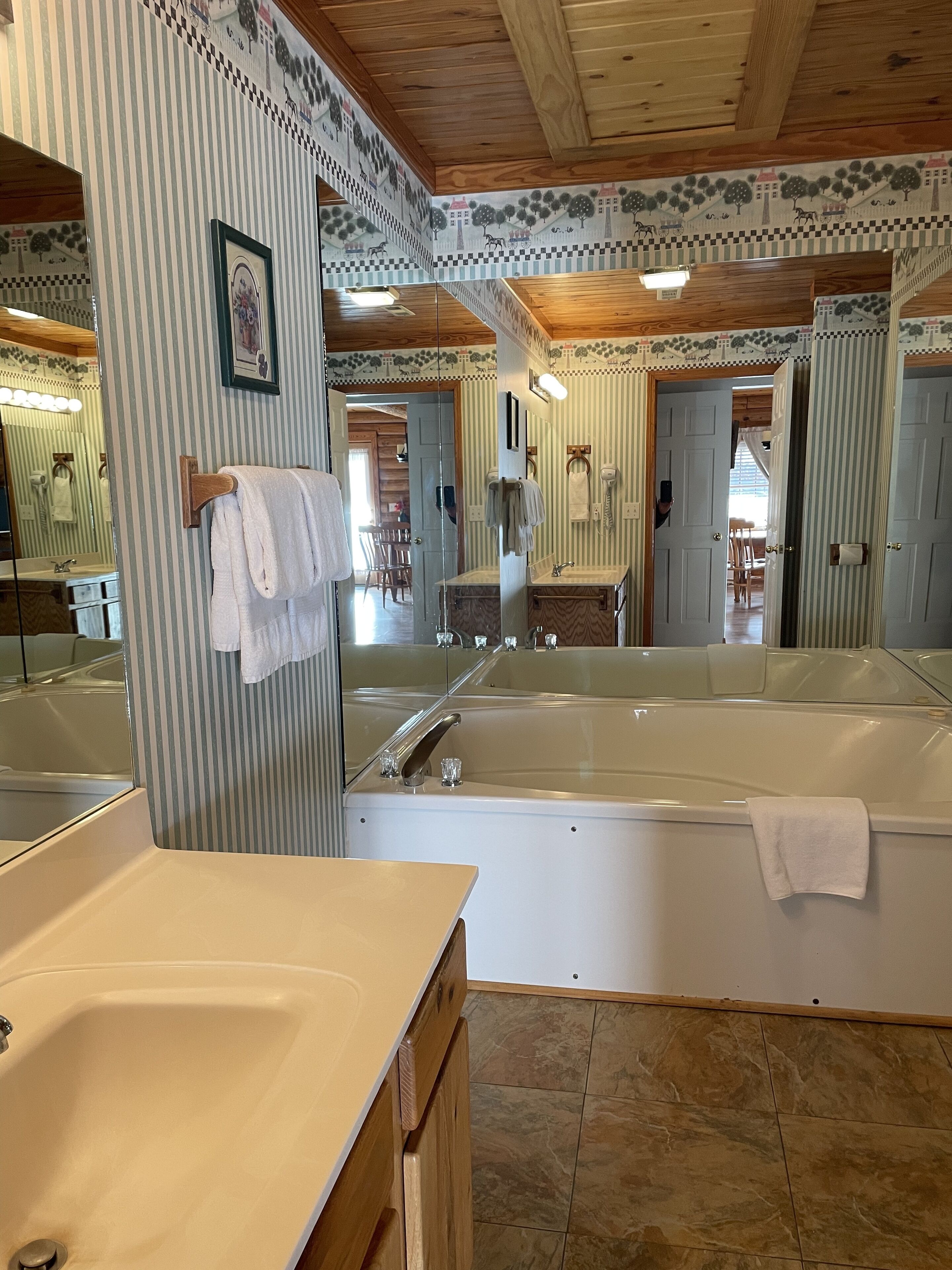 A bathroom with a large mirror, a bathtub, a sink, and a wooden vanity.