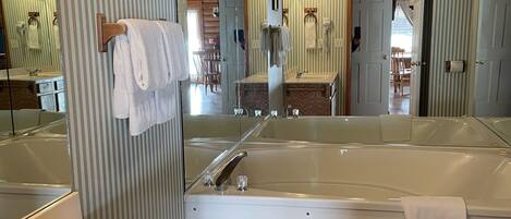 A bathroom with a large mirror, a bathtub, a sink, and a wooden vanity.