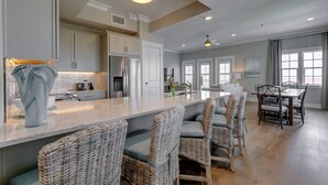 A modern kitchen with a central island, wicker chairs, and a dining area with a table and chairs. - Spa Escape Seaside Bliss | Luxe Haven for 8 (Destin)