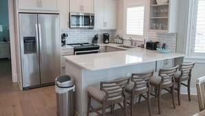 A modern kitchen with white cabinetry, stainless steel appliances, a central island with bar stools, and a microwave above the counter.