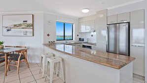 Uma cozinha moderna com uma ilha grande, eletrodomésticos de aço inoxidável e vista para o oceano.
